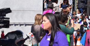 Woman talking into Telemundo news microphone & camera holding sign that reads "CHILDREN MATTER"