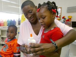 A teaching assistant helps a child with glue at Redwood Early Learning Center in North Little Rock, Arkansas.